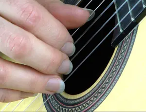Classical guitarist playing nylon-string guitar using fingernails for nail picking technique